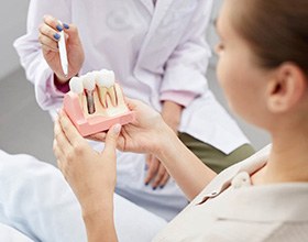 A dentist using a dental implant model to explain treatment to a patient