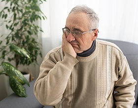 Older man in sweater sitting on couch with tooth pain