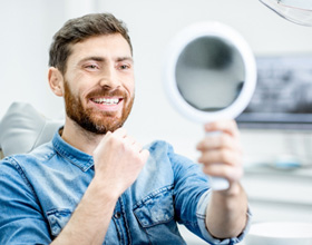 Male dental patient checking smile in handheld mirror