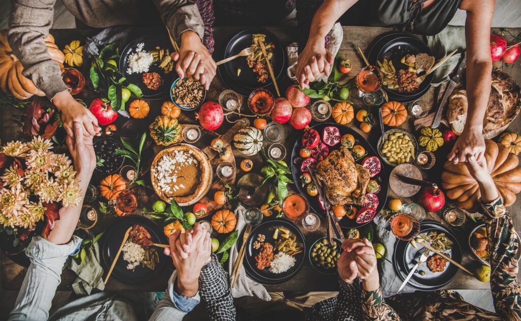 Bird's eye view of hands held around a large table full of Thanksgiving foods